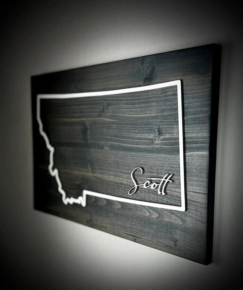 The Large Rectangle Personalized MT Sign by B. James Design & Woodwork features Montana’s outline and custom name on a dark wooden background—perfect for any space. Custom colors available.