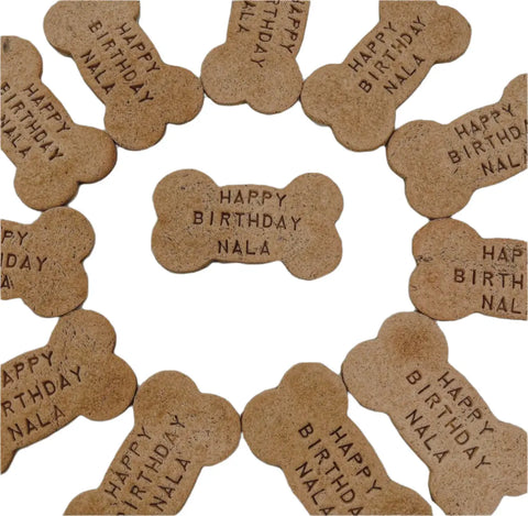 A dozen Personalized Bone Cookies by Dogtown Bakery arranged in a circle with one in the center, each stamped with HAPPY BIRTHDAY NALA on a white background—handcrafted treats perfect for your pup’s special day.