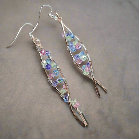 DNA Strand Double Helix Long Crystal Earrings by Alexa Martha Designs feature elegant leaf shapes, wire wrapping, and pastel crystals in purple, blue, green, and pink—beautifully showcased on a neutral background.