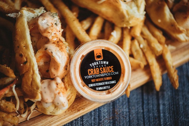 Container of Yorktown Crab Sauce with seafood and fries on a board