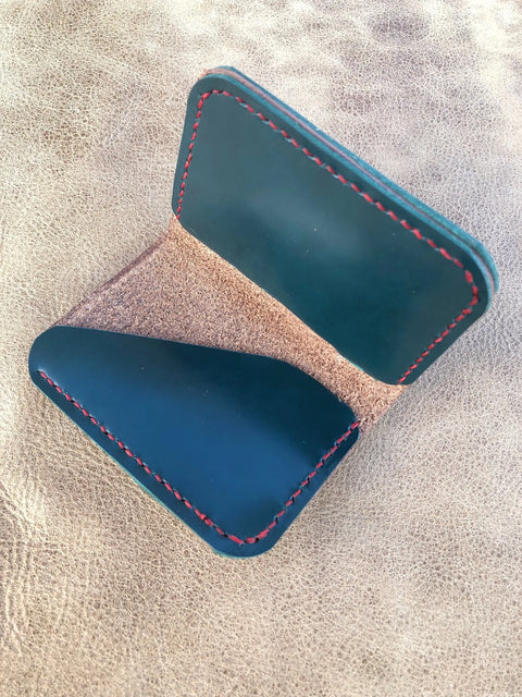 The Sully + Proper Supply Dark Sea Teal Card Wallet With Buffalo Nickel, crafted from blue leather with red stitching and a suede-like interior, is shown open on a textured beige surface.