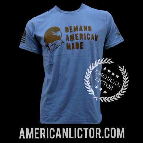 The T-Shirt: Demand American Made by American Lictor features a light blue color, eagle graphic, and DEMAND AMERICAN MADE text on the front. Logo and americanlictor.com displayed below. Check our Size Guide for your perfect fit.