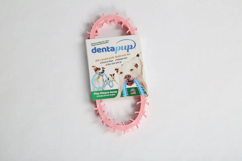The Dentapup Dog Dental Toy - Pink by Dentapup is an oval-shaped toy in branded packaging with a photo of a playful dog and text highlighting its dental hygiene benefits and effective plaque and tartar removal for pets.