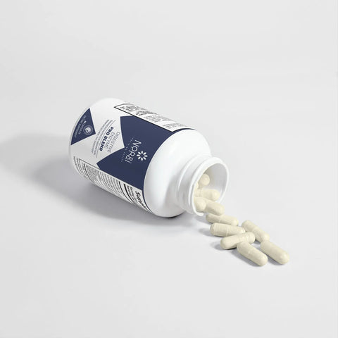 A white bottle labeled Norri Nutrition Digestive Enzyme Pro Blend lies on its side, several white capsules spilling onto a white surface. The dark blue and white label highlights its focus on digestive health—formulated to support nutrient absorption.