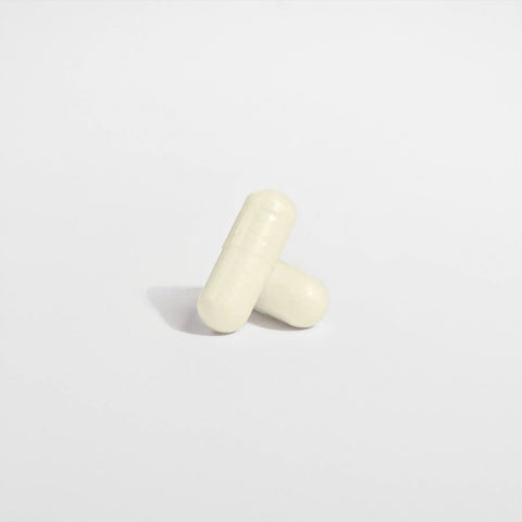 Two white capsules of Norri Nutrition’s Digestive Enzyme Pro Blend stand upright on a plain white background, one gently leaning on the other—symbolizing support for digestive health and better nutrient absorption.