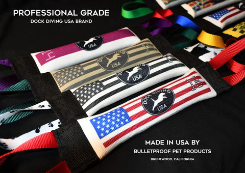 Four Dock Diving Bumper Tug - Competition Series Weighted toys by Bulletproof Pet Products Inc, each customizable with patriotic themes and the “Dock Diving USA” logo, are lined up to highlight their USA-made quality and weighted dock diving bumper design.