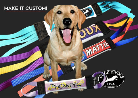 A cheerful yellow Lab sits before four Dock Diving Bumper Tug - Competition Series Weighted toys, each with custom names and colors. Text says MAKE IT CUSTOM! with Duck Diving USA logos. Trusted quality from Bulletproof Pet Products Inc.