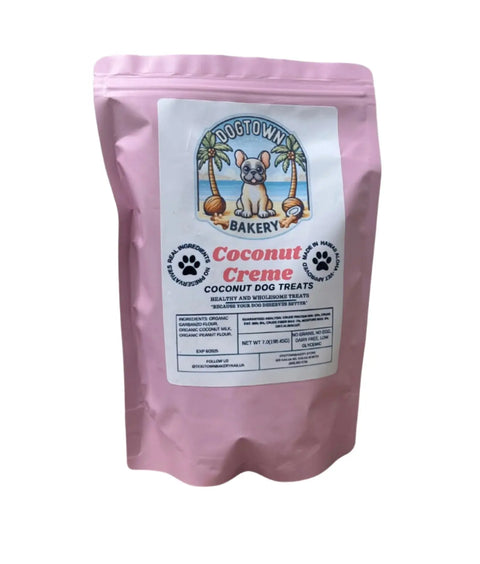 A pink resealable bag of Dogtown Bakery Coconut Creme Biscuits hypoallergenic dog treats displays an illustrated dog and palm trees on the label, with product details below.