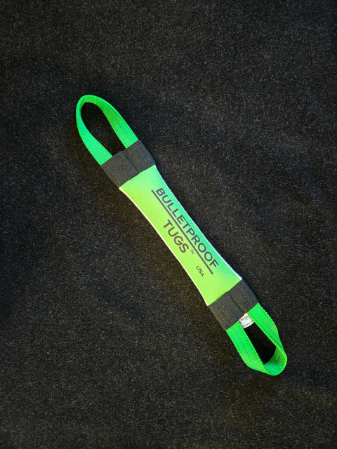 The Doing Bad Dog Shit Fire Hose Training Tug (Bad Tug Line) by Bulletproof Pet Products Inc is a green and black heavy-duty dog toy with BULLETPROOF TUGS printed on it, featuring two looped handles for tugging.