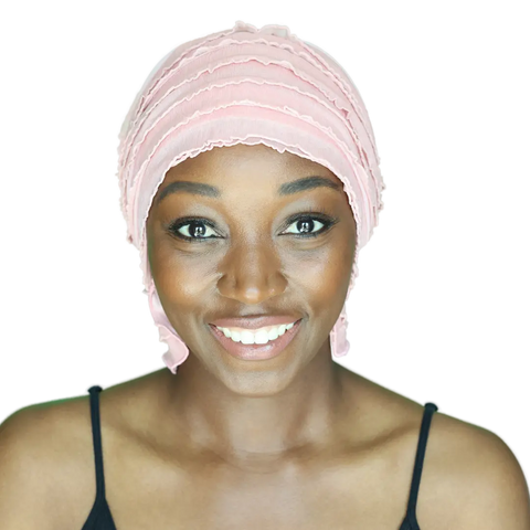 A woman smiles at the camera, wearing the Chemo Beanies® Donna pink ruffled chemo beanie and a black spaghetti strap top, against a white background.