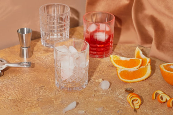 Cocktail setup with glasses, ice, and orange slices on a wooden surface.