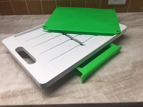 The Karving King Dripless Cutting Board 2 in 1 System, featuring a white board with handle, green flexible mat, and green slide-out drip tray, sits on a marble countertop.