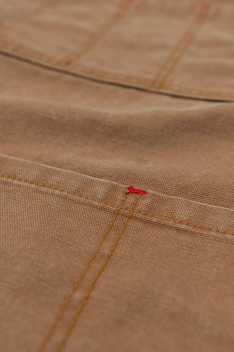 Close-up of The Common Apron Canvas by Marc Nelson, showing tan denim fabric with yellow and red stitching along the seams, highlighting its textured material, fine sewing details, and multiple pockets.