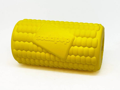 The SodaPup Corn on the Cob EDispenser is a durable yellow rubber chew toy for dogs with detailed kernel textures, a cylindrical shape, and a treat-dispensing feature. SodaPup is embossed on a rectangular patch in the center.