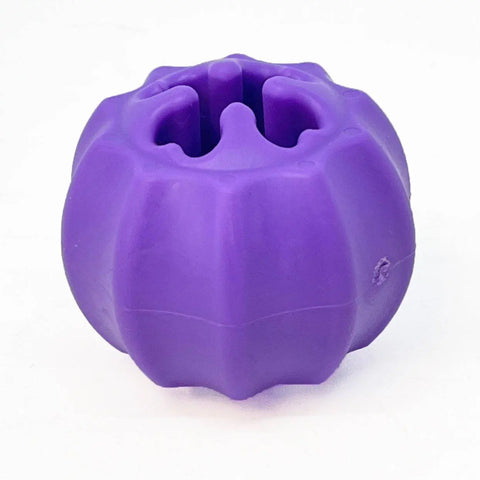 The SodaPup Cross Bones Chew Toy and Treat Pocket is a round, ridged, bright purple rubber toy with wavy openings and a hollow center, designed to dispense treats or hold bully sticks for interactive dog play.
