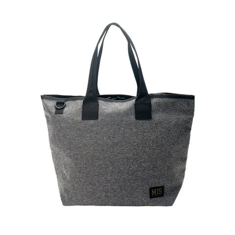 The MIS Tote Bag - Denim Grey is crafted from Cordura nylon, features black handles, a black MIS logo patch near the bottom corner, and a metal ring by one handle. This water-resistant bag has a simple, minimalist design.