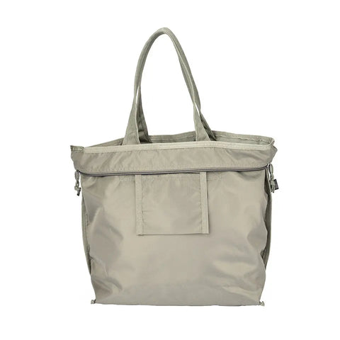 The MIS Tote Bag - Denim Grey is made from water-resistant Cordura nylon and features two handles, a front pocket, zippered top, and minimalist design. This spacious tote is practical and stylish in light gray.