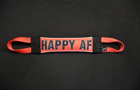 A Bulletproof Pet Products Inc Happy AF Fire Hose Training Tug with loops at both ends lies on a black surface. The heavy-duty dog toy’s center panel reads HAPPY AF in bold letters. Proudly made in the USA.