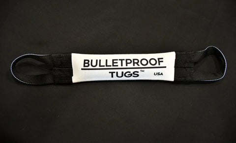 A black and white Daddys Girl Fire Hose Training Tug by Bulletproof Pet Products Inc lies on a black surface, featuring loops on both ends and bold BULLETPROOF TUGS™ USA text, highlighting this durable, USA-made dog toy.