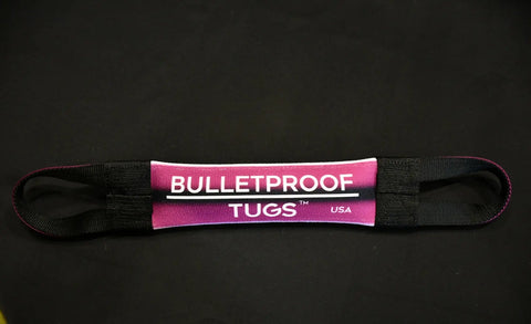 A pink and black Crazy Bitch Fire Hose Training Tug by Bulletproof Pet Products Inc lies on a black surface. Built in the USA with two strong black handles, this durable tug is perfect for tough play and dependable training.