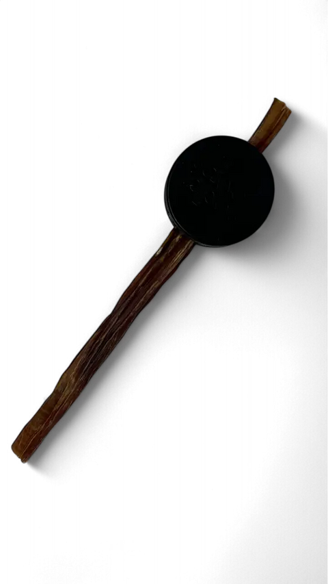 A SodaPup Hockey Puck Durable PUP-X Rubber Treat Holder and Chew Toy is balanced on a long, brown, dried stick against a black background.