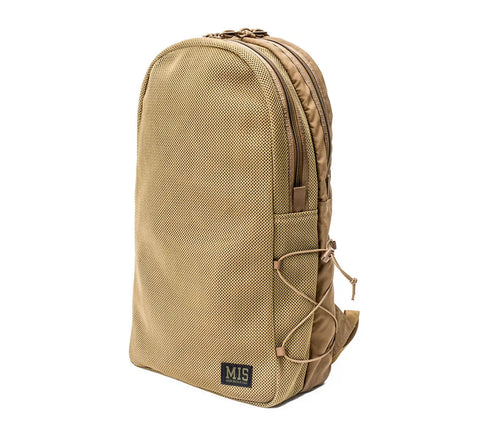 The MIS Mesh Backpack - Coyote Brown is a 19L Cordura Nylon laptop backpack made in the USA, featuring textured fabric, a front zipper pocket, side cord details, and a black MIS patch on the lower front. It stands upright on a white background.
