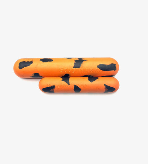 Two Goughnuts Orange Stick dog toys, featuring an orange cylindrical design with irregular black spots like a tiger pattern, are placed side by side on a white background. One toy is larger than the other.