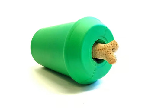 A SodaPup Coffee Cup EDispener, a green durable rubber chew toy and treat dispenser, holds a bone-shaped dog treat partially sticking out from its round opening, set against a white background.