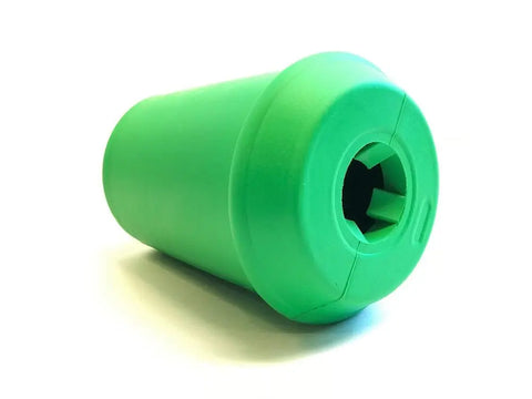 The SodaPup Coffee Cup EDispenser is a green, cylindrical durable rubber chew toy and treat dispenser with a wide rounded cap and cross-shaped opening, shown resting on a white surface.