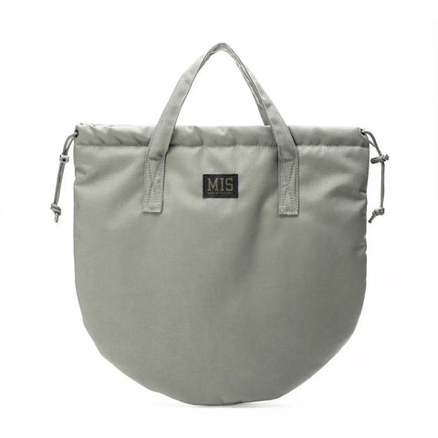 The MIS UK Helmet Bag - Foliage is a light gray, rounded Cordura Nylon bag with short handles, side drawstrings, and a black patch with gold MIS lettering, shown on a plain white background.