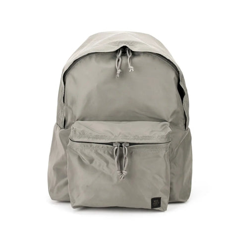 The MIS Daypack - Foliage is a light gray, water-resistant nylon backpack featuring a spacious main compartment, front zippered pocket, two side pockets, drawstring pulls, and a small black label on the front pocket’s bottom right corner.