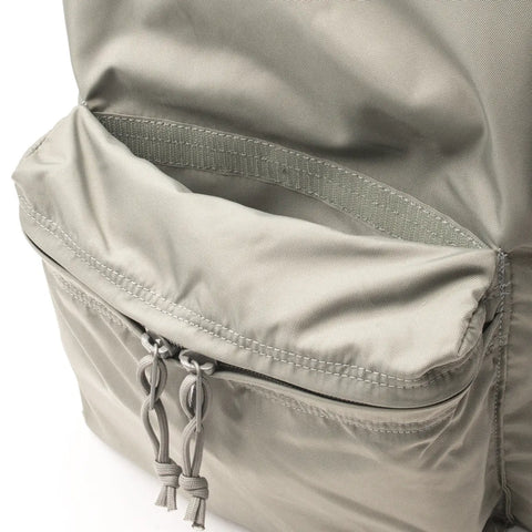 A close-up of the MIS Daypack - Foliage in light gray nylon shows two knotted cord zipper pulls and an open top compartment, highlighting its smooth, water-resistant fabric texture.
