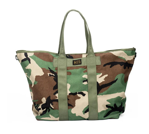 The MIS Super Tote Bag - Woodland Camo is a large Cordura nylon tote with green handles, water-resistant material, a front MIS label, woodland camouflage pattern, and a top zipper closure.
