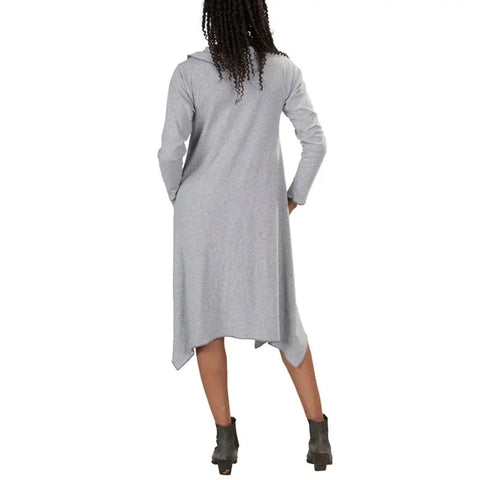 A woman with long braids, seen from behind, models the Spiritex 50/50 Long Sleeve Colette Drape Dress—a light gray organic cotton dress with an uneven hem and A-line silhouette—paired with dark ankle boots against a white background.