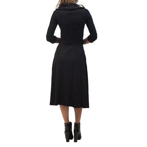 A woman models the Spiritex French Broad Dress, a knee-length black organic cotton style with three-quarter sleeves, and black ankle boots, facing away to showcase the back of the outfit against a white background.