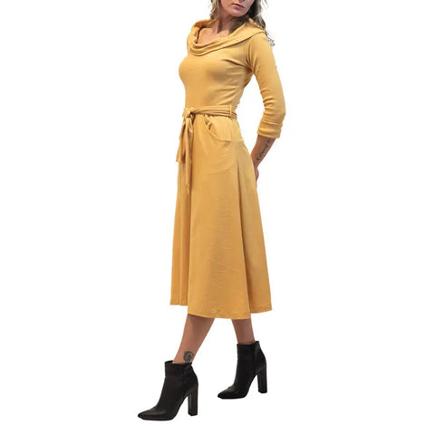 A woman models the Spiritex | Sustainable Apparel French Broad Dress, a 50s-inspired mustard yellow belted midi with a cowl neckline, paired with black ankle boots, against a white background.