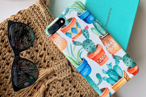 Phone case with cactus design, sunglasses, and Tiffany & Co box on a textured surface