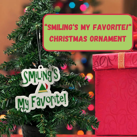 A small Christmas tree displays Chatelet Manufacturing’s Elf Christmas Ornament, featuring Buddy the Elfs saying “Smiling’s My Favorite!” beside a red gift. Text reads: “‘SMILING’S MY FAVORITE!’ CHRISTMAS ORNAMENT.”.