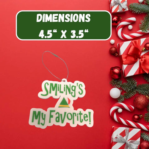 The Chatelet Manufacturing Elf Christmas Ornament features Smilings My Favorite!—a festive Buddy the Elf saying. Displayed on a red background with gifts, candy canes, and pine branches. Dimensions: 4.5 x 3.5 in. Made in USA.