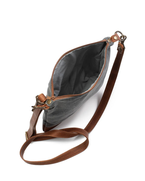 The Ellis River Crossbody Bag by Rogue Industries is a small gray canvas bag with a brown leather strap and brass hardware, shown open to display its lined interior against a white background.