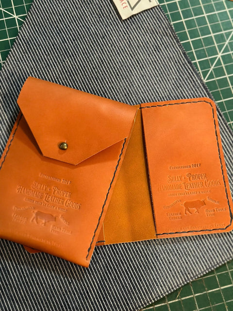 The Sully + Proper Supply Travel Bundle, featuring a Utility Pouch and Passport Cover, is displayed on striped fabric and a green cutting mat. Both items are American-made leather goods established in 2017.