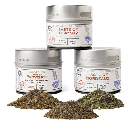 The Gustus Vitae Italian and French Countryside Spice Blend Collection features three tins stacked on a white background, each with dried herbs and spices in front, creating a gourmet gift set.