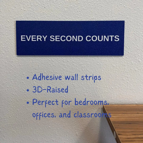 A blue Chatelet Manufacturing Every Second Counts Wall Sign decorates a white wall, featuring 3D-raised details and adhesive strips. Ideal for kitchens, bedrooms, offices, or classrooms. A wooden surface is visible at lower right.