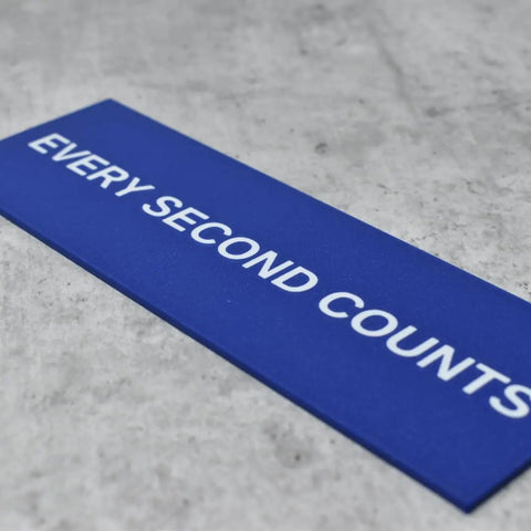 A blue rectangular Every Second Counts Wall Sign by Chatelet Manufacturing with white text sits on a light gray textured surface—a stylish inspirational kitchen decoration perfect for fans of The Bear wall sign.