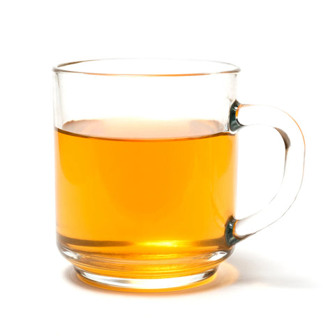 A clear glass mug of Sasquatch Tea Co’s Exotic Everglades Rooibos Fruit Tea, light amber in color, sits on a white background.