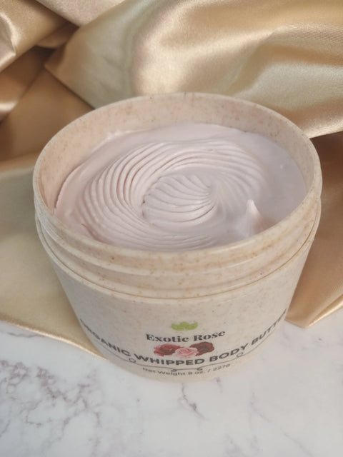 An open jar of Forev'Herbs Exotic Rose Organic Whipped Body Butter with a swirled pink surface sits on marble beside gold satin fabric, highlighting this luxurious, organic whipped body butter.
