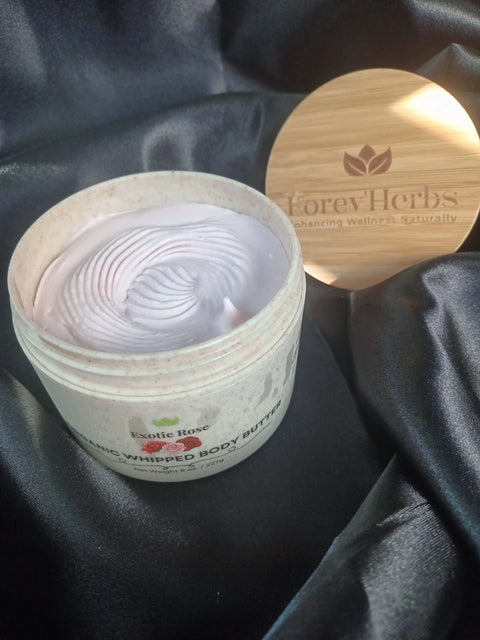 An open jar of Exotic Rose Organic Whipped Body Butter displays its creamy swirl on black satin. The wooden lid, branded Forev'Herbs, rests beside it—highlighting the luxurious essence of this nourishing body butter.