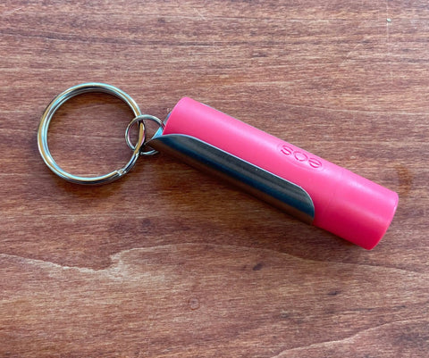 A Tallac House Lip Balm Keychain Xtra-Large Lip Balm Holder, USA Made with stainless steel, fits larger diameter lip balms only. Its a stylish holder for easy on-the-go access, shown here on a wooden surface.