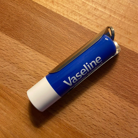 A Tallac House Xtra-Large Lip Balm Holder for larger lip balms, made in the USA, with a stainless steel keychain and metal clip, rests on a wooden surface.