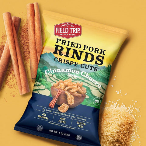 Field Trip Cinnamon Churro 1oz (6 Pack) Fried Pork Rinds are shown on a yellow background with cinnamon sticks and brown sugar. The packaging highlights all natural, airy puffs that are gluten free and Keto friendly.